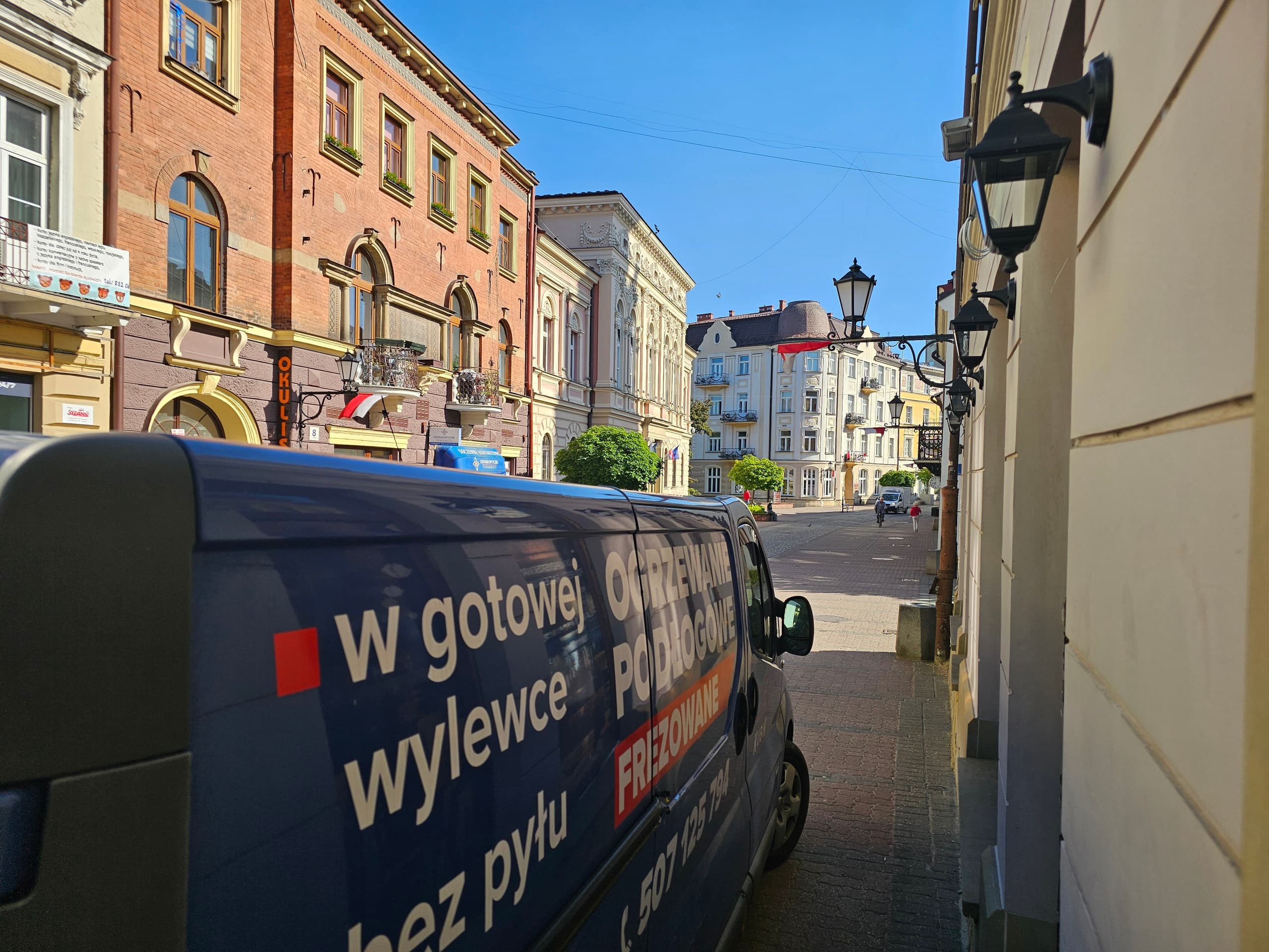 Kubik's blue van with the lettering “Milled underfloor heating”, parked on a town square